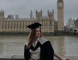 Elmira in a graduation gown by the Thames, with Big Ben behind her